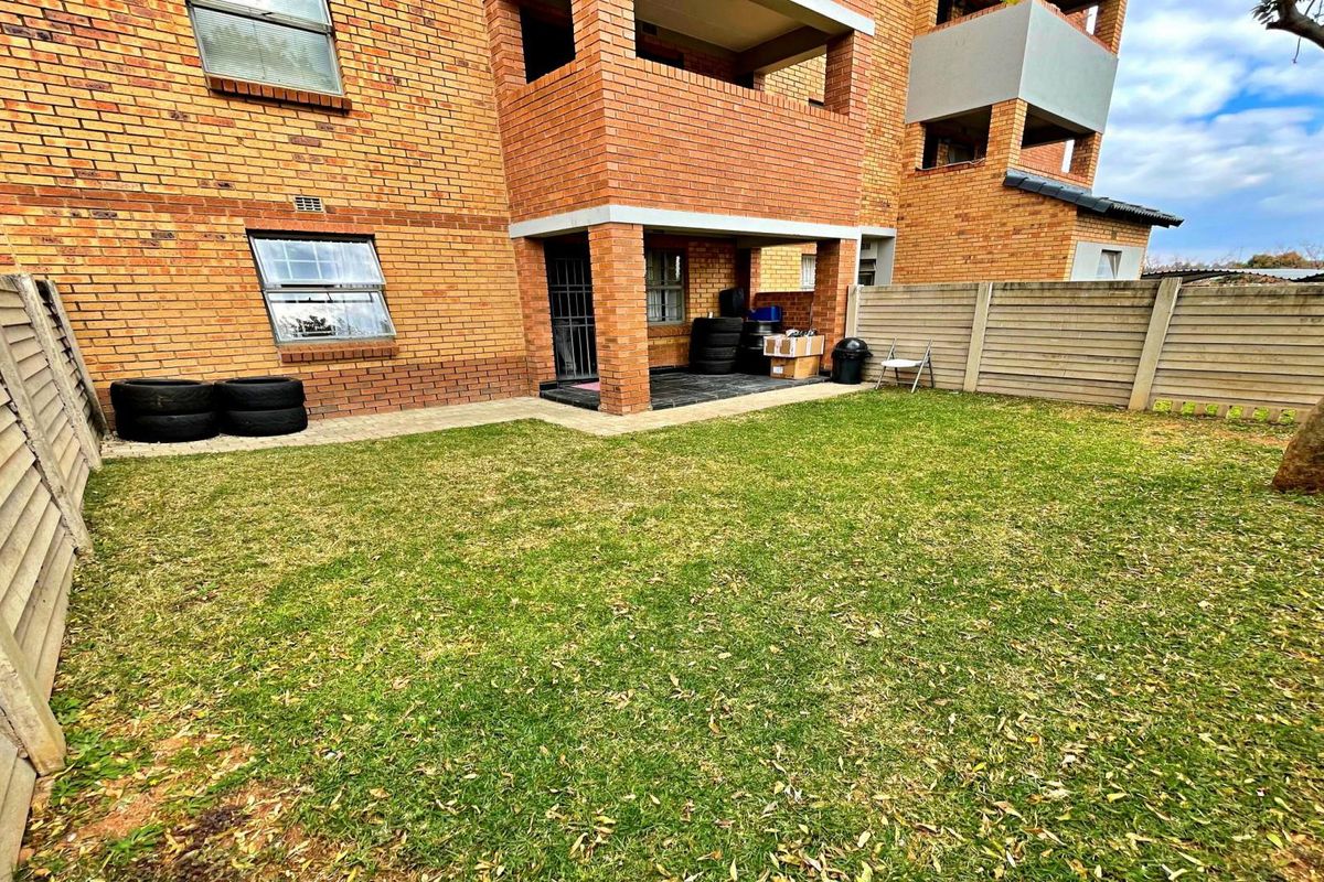 A private rear garden area featuring a lawn, precast concrete boundary walls, and a covered patio attached to the brick apartment building.