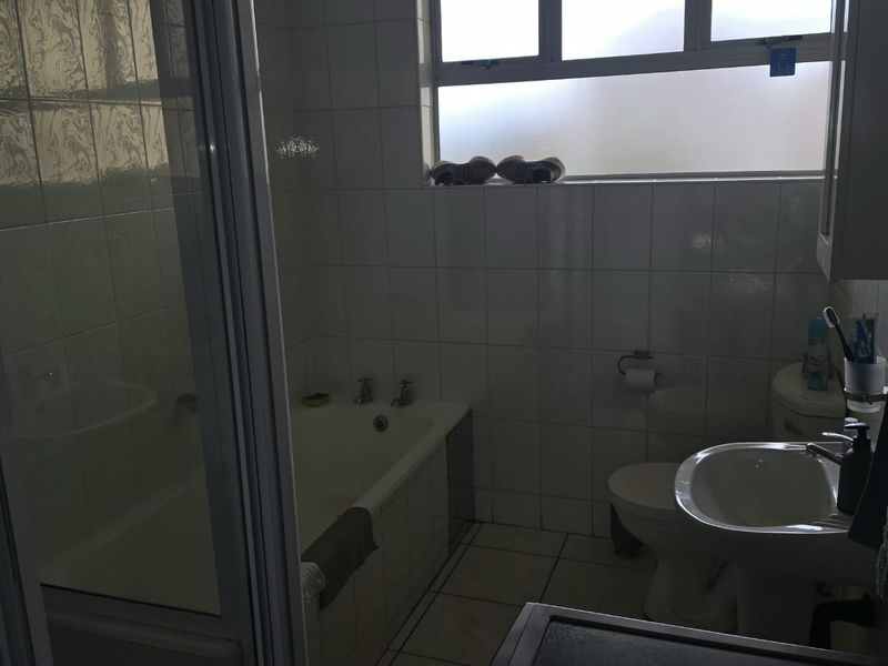 A functional bathroom featuring a bathtub, separate shower enclosure, pedestal basin, and toilet with tiled finishes and a frosted window for natural light.