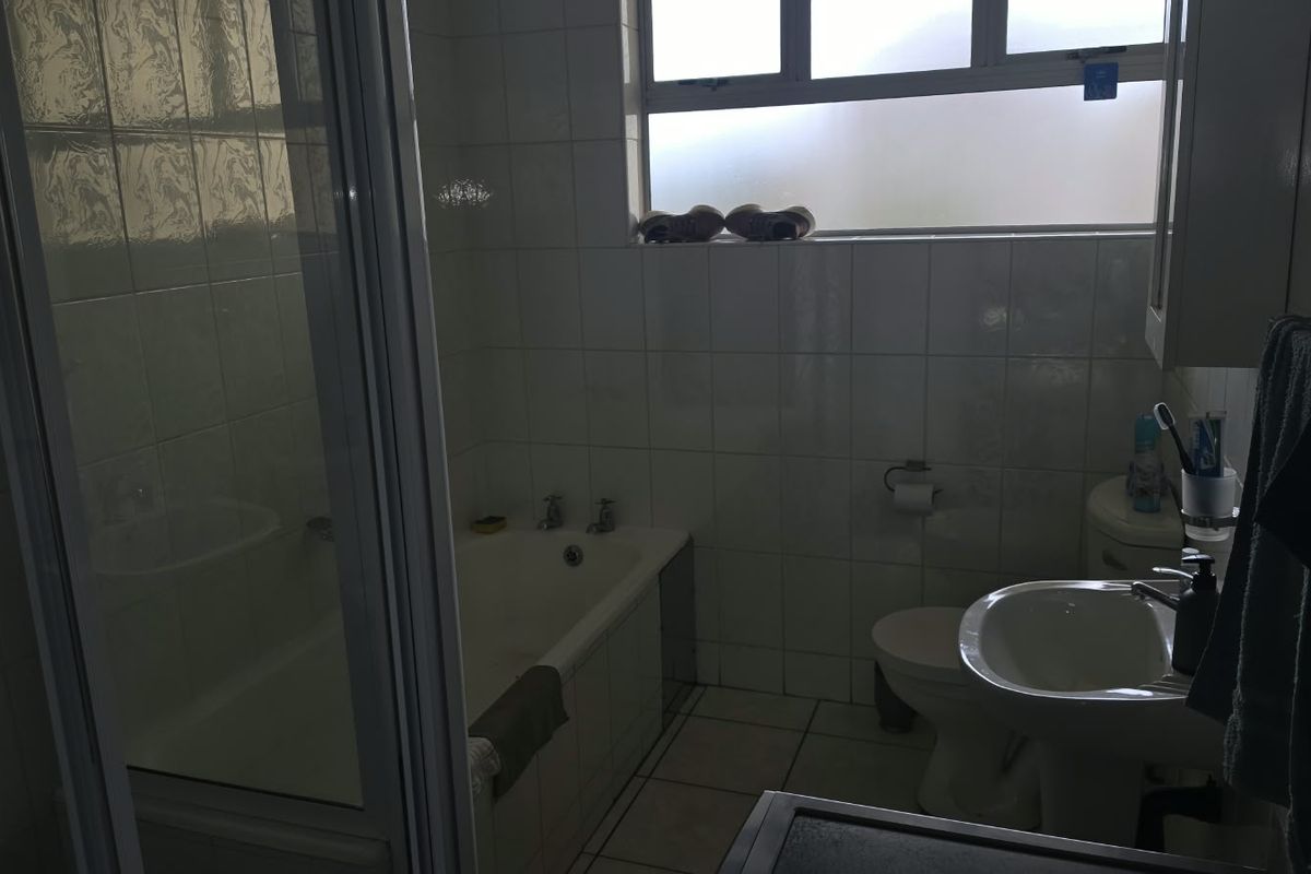 A functional bathroom featuring a bathtub, separate shower enclosure, pedestal basin, and toilet with tiled finishes and a frosted window for natural light.
