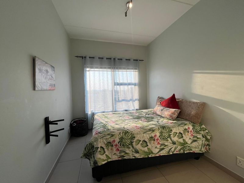 A functional bedroom featuring tiled flooring, a large sliding window for natural light, and a wall-mounted television bracket.