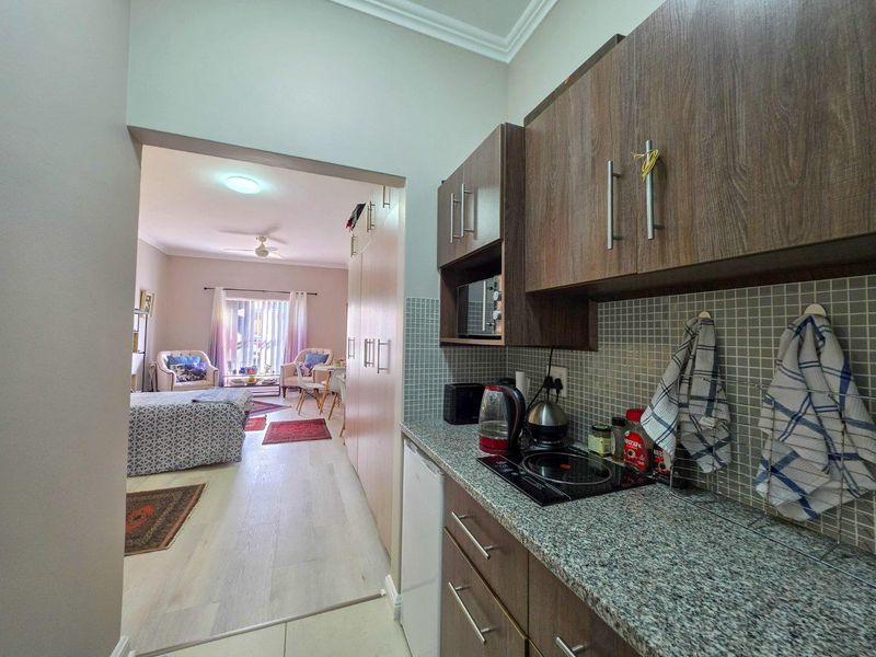Open-plan living area featuring a compact kitchenette with granite countertops, mosaic backsplash, and built-in cabinetry, flowing into a comfortable living and sleeping space.