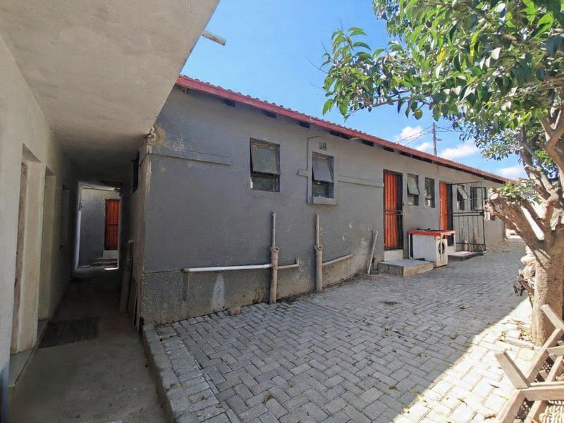 Rear exterior view of the property featuring a paved courtyard, security gates, and external wall finishes requiring maintenance.