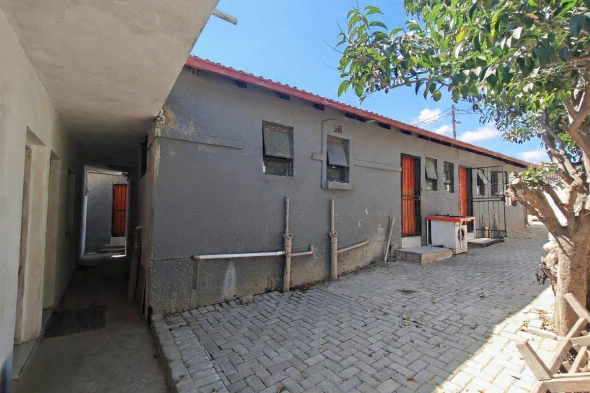 Rear exterior view of the property featuring a paved courtyard, security gates, and external wall finishes requiring maintenance.