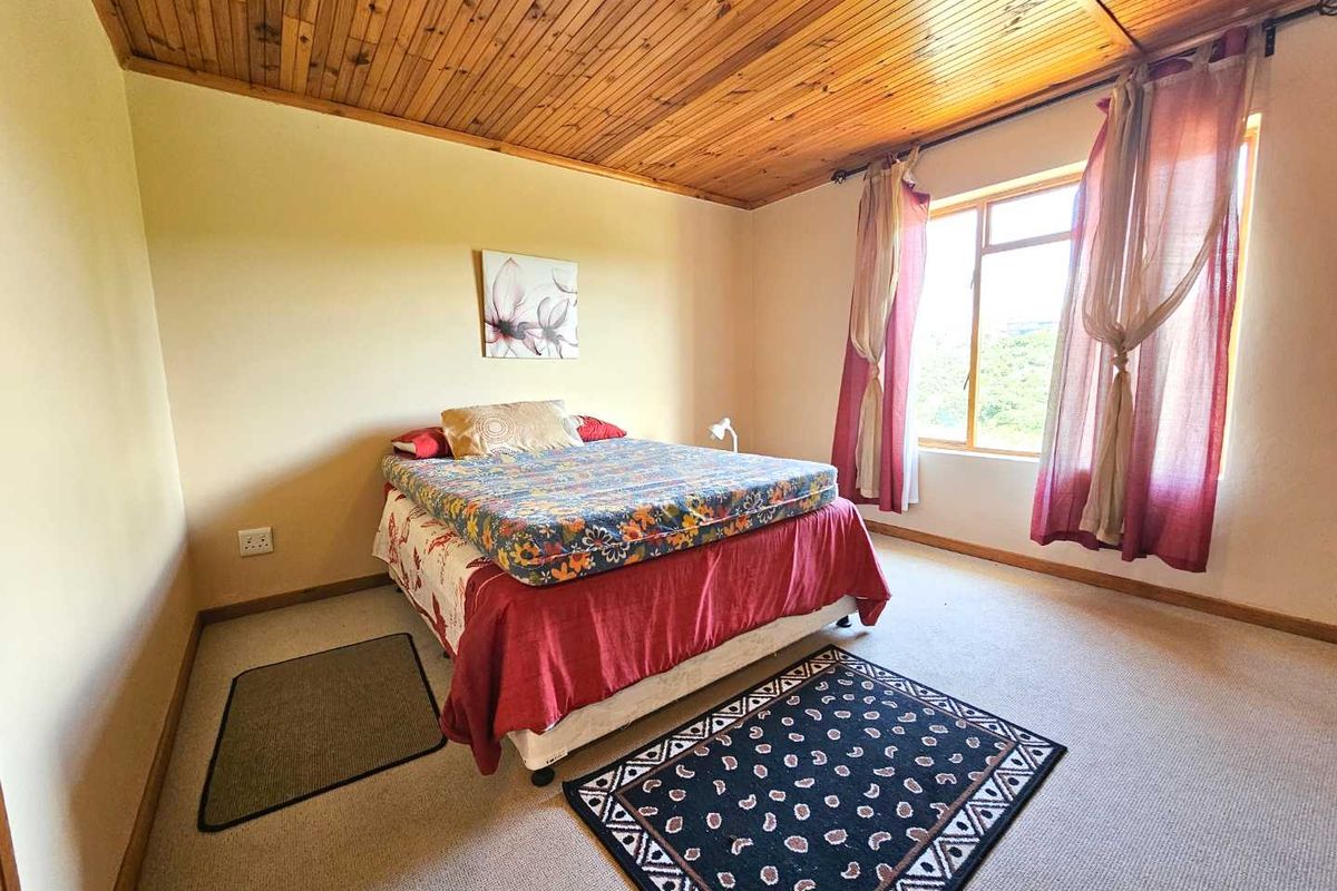A bedroom featuring a timber-clad ceiling, neutral walls, and carpeted flooring, with a large window providing natural light.