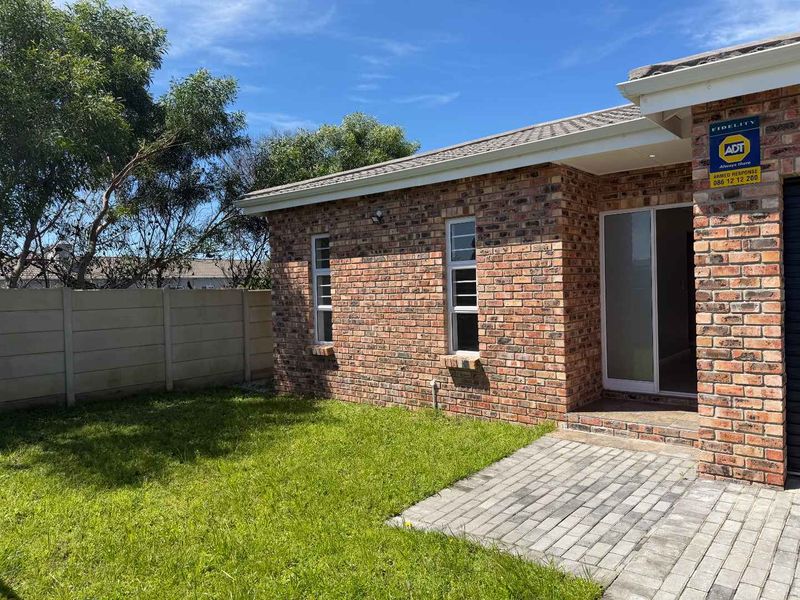 Rear view of a face brick house featuring a paved patio area, neat lawn, and secure boundary walling.