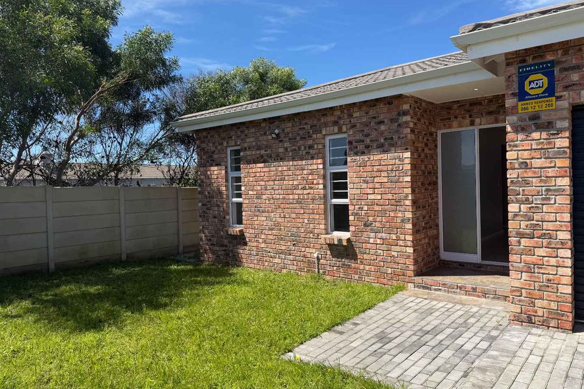 Rear view of a face brick house featuring a paved patio area, neat lawn, and secure boundary walling.