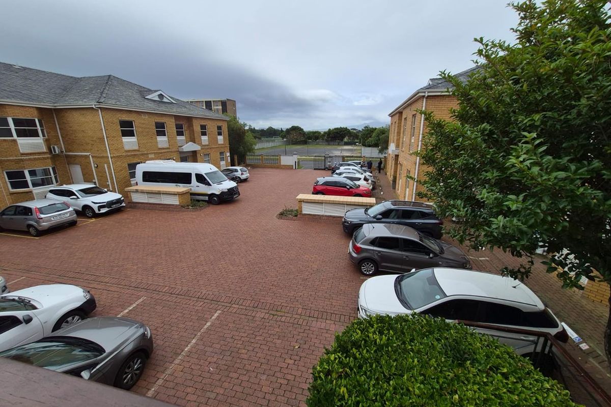 An elevated view of a paved parking courtyard situated between two brick office buildings, featuring designated parking bays and perimeter security fencing.