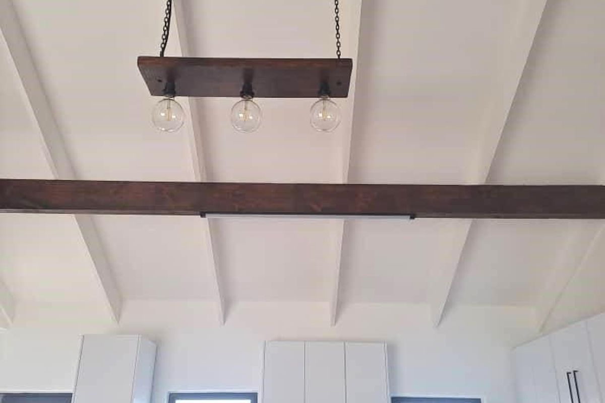 Modern kitchen featuring white cabinetry, subway tile backsplash, and exposed timber ceiling beams with industrial-style pendant lighting.