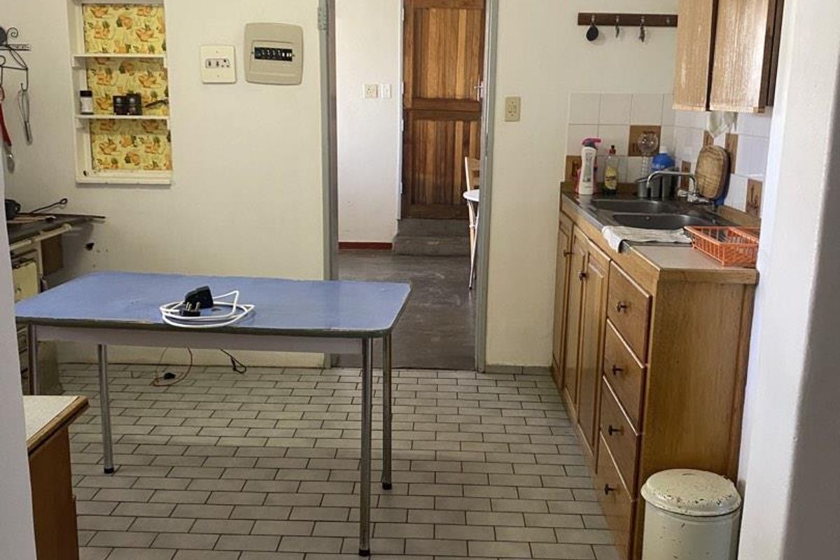 A functional kitchen featuring wooden cabinetry, tiled flooring, and a built-in sink, providing a practical layout with direct access to an adjacent room.