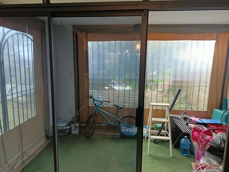 Enclosed patio area featuring sliding glass doors, artificial turf flooring, and protective outdoor blinds, offering a versatile space for outdoor living.