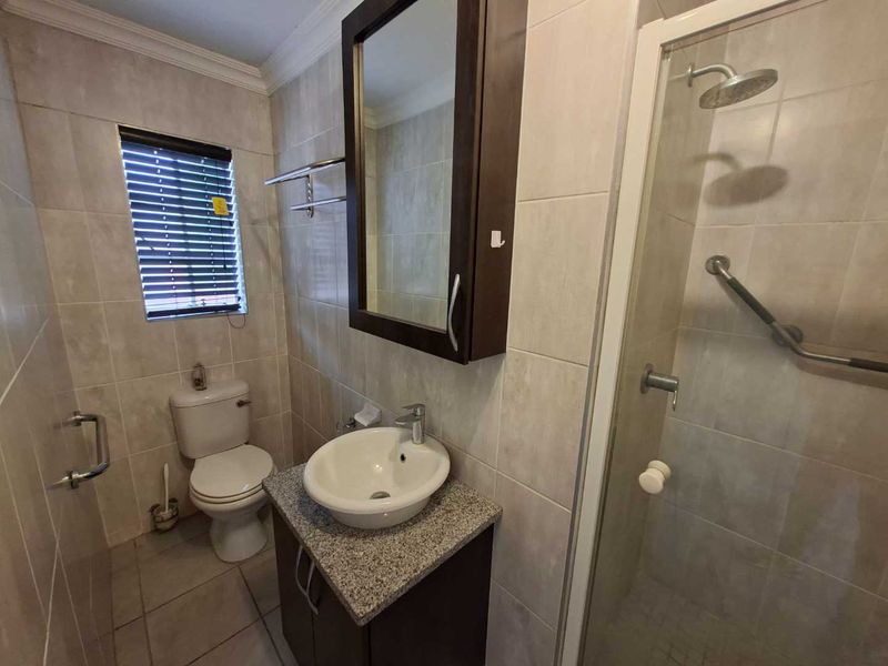 A functional bathroom featuring a vanity with granite countertop, vessel sink, wall-mounted medicine cabinet, and a glass-enclosed shower with grab bars.