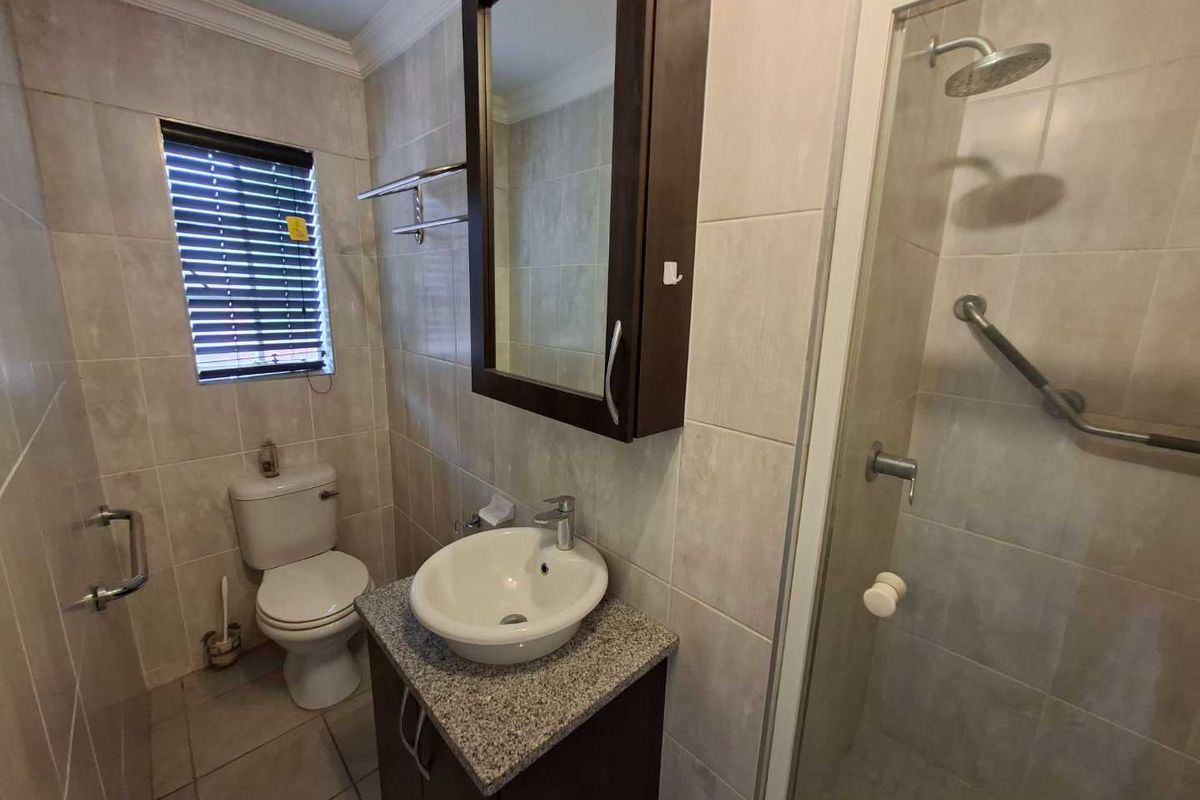 A functional bathroom featuring a vanity with granite countertop, vessel sink, wall-mounted medicine cabinet, and a glass-enclosed shower with grab bars.