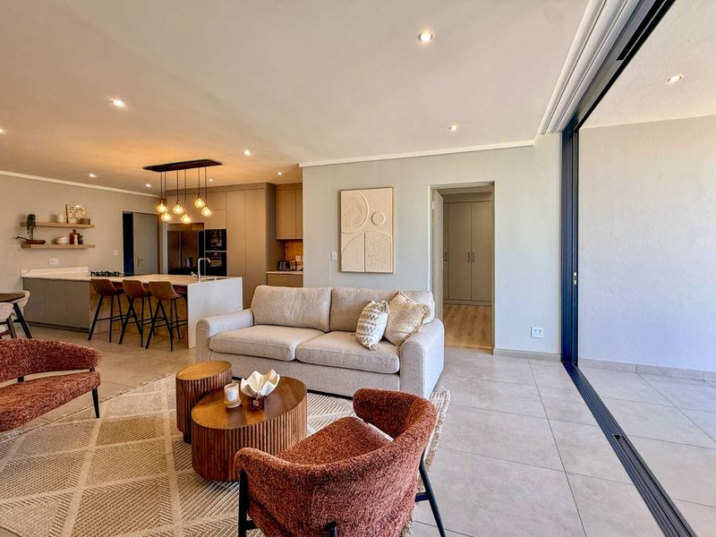 Modern open-plan living area featuring a sleek kitchen with island, recessed lighting, and large sliding doors opening to an outdoor space.