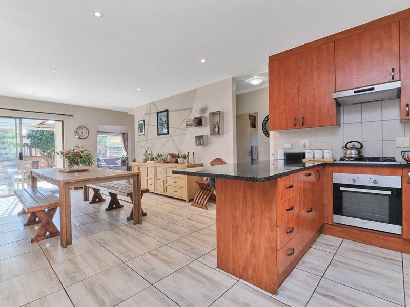 Open-plan kitchen and dining area featuring wood-finish cabinetry, granite countertops, built-in appliances, and tiled flooring with direct access to the outdoor patio.