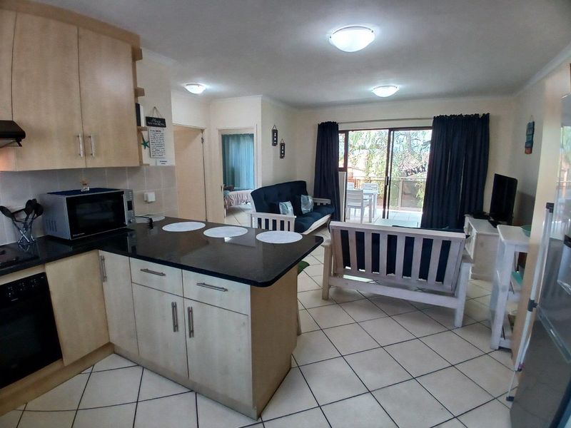 Open-plan living area featuring a functional kitchen with granite countertops, tiled flooring, and direct access to a private balcony through sliding glass doors.