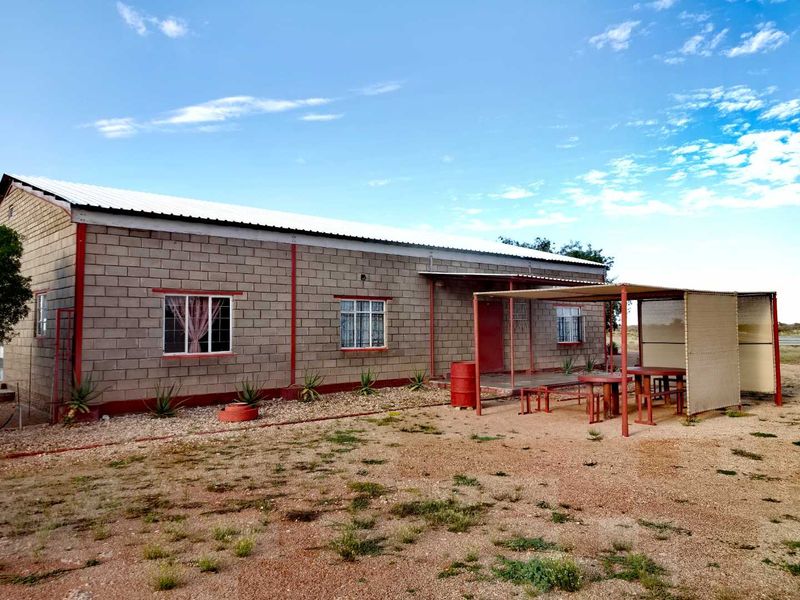 Rear view of a farm-style building featuring concrete block construction, a corrugated metal roof, and a covered outdoor patio area.