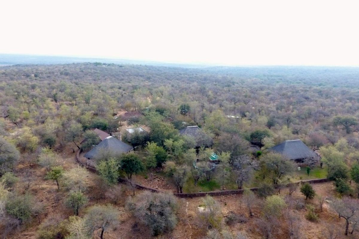 Aerial view of a property complex featuring multiple structures with thatched roofs, situated within a natural bushveld landscape.