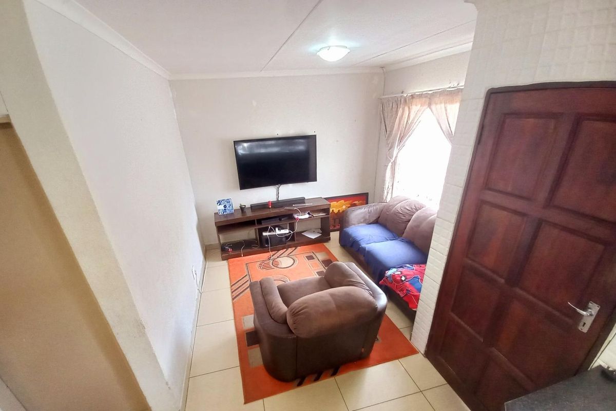 A compact living room featuring tiled flooring, a ceiling-mounted light fixture, and a window with curtain tracks.