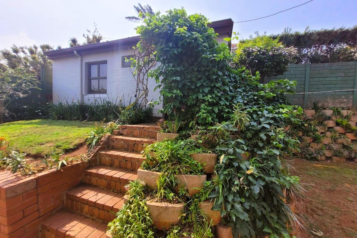 A rear garden view featuring brick stairs leading to the house, surrounded by established landscaping and retaining wall planters.