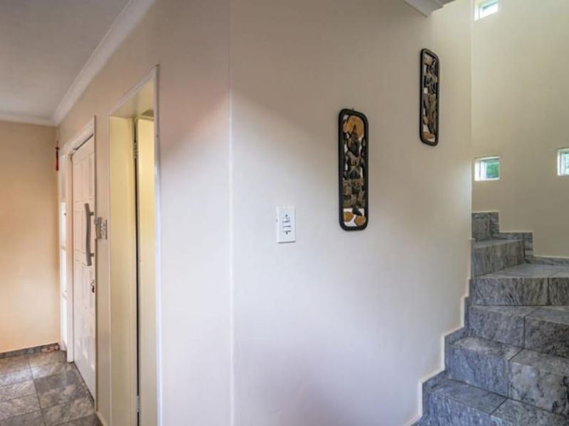 A bright, tiled hallway featuring a staircase with stone-look steps and multiple small windows providing natural light.