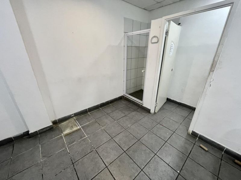 An empty industrial-style bathroom featuring tiled flooring and a separate shower enclosure with tiled walls.