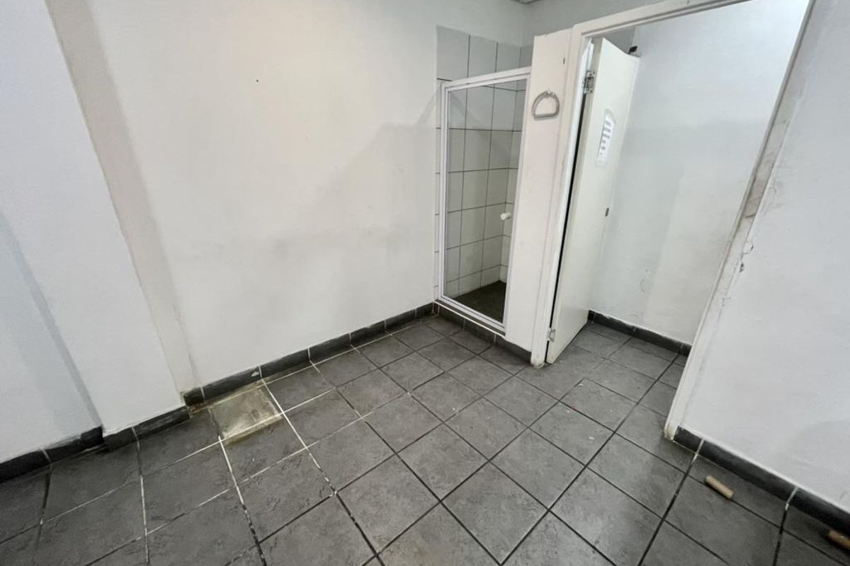 An empty industrial-style bathroom featuring tiled flooring and a separate shower enclosure with tiled walls.