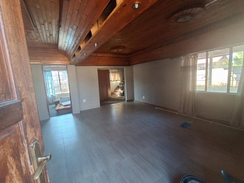 Spacious living area featuring a distinctive timber-clad vaulted ceiling and modern tiled flooring, currently vacant and awaiting finishing touches.