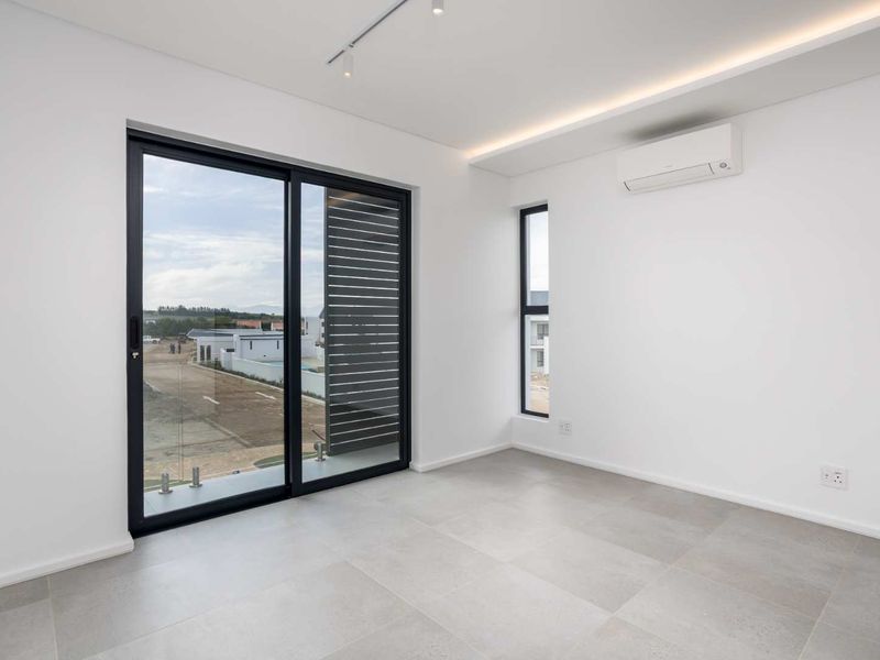A bright, modern, and empty bedroom featuring large sliding glass doors, tiled flooring, and a wall-mounted air conditioning unit.