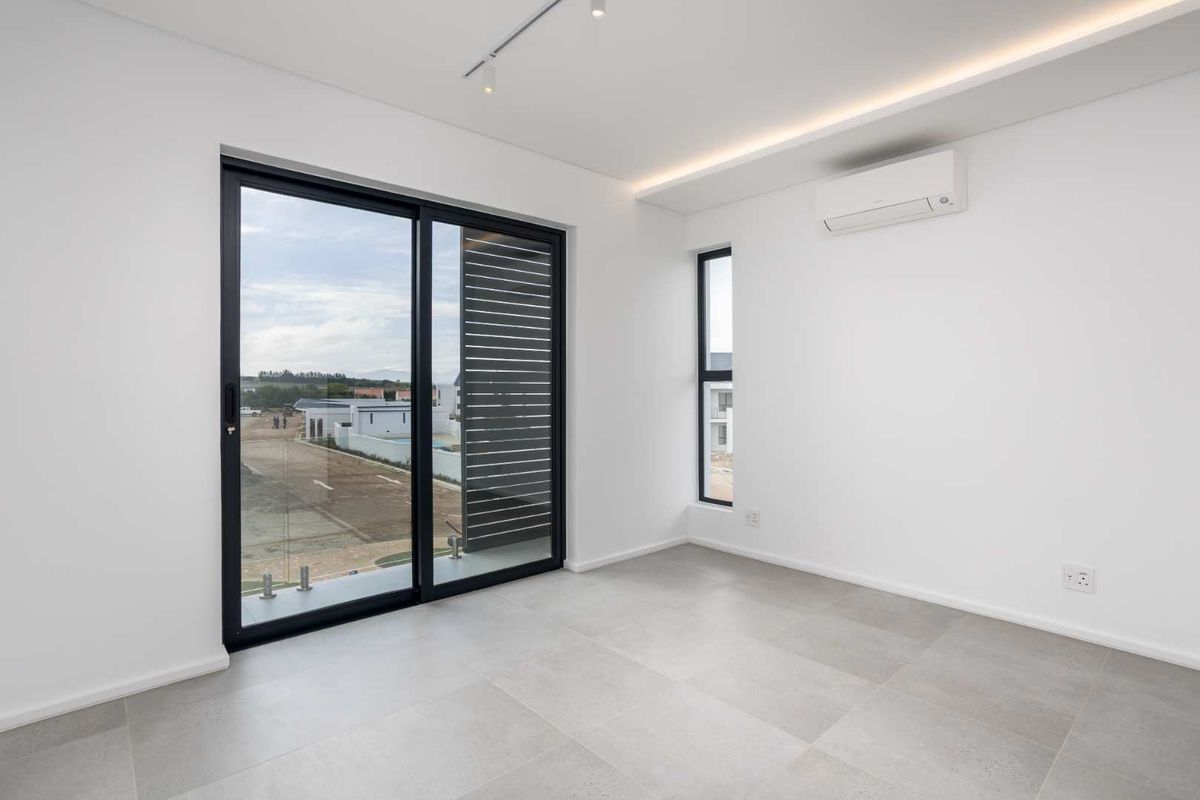 A bright, modern, and empty bedroom featuring large sliding glass doors, tiled flooring, and a wall-mounted air conditioning unit.