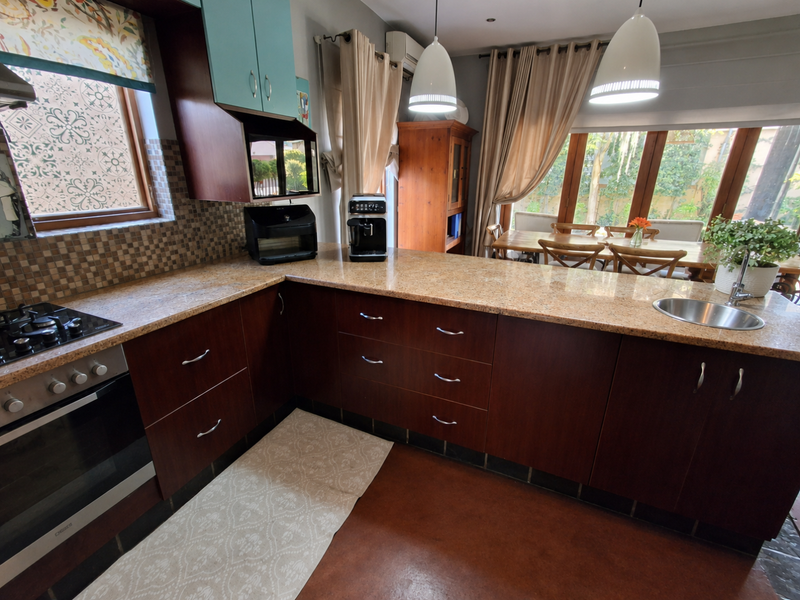 A functional kitchen featuring dark wood cabinetry, granite countertops, a built-in oven with gas hob, and a stainless steel sink overlooking the dining area.