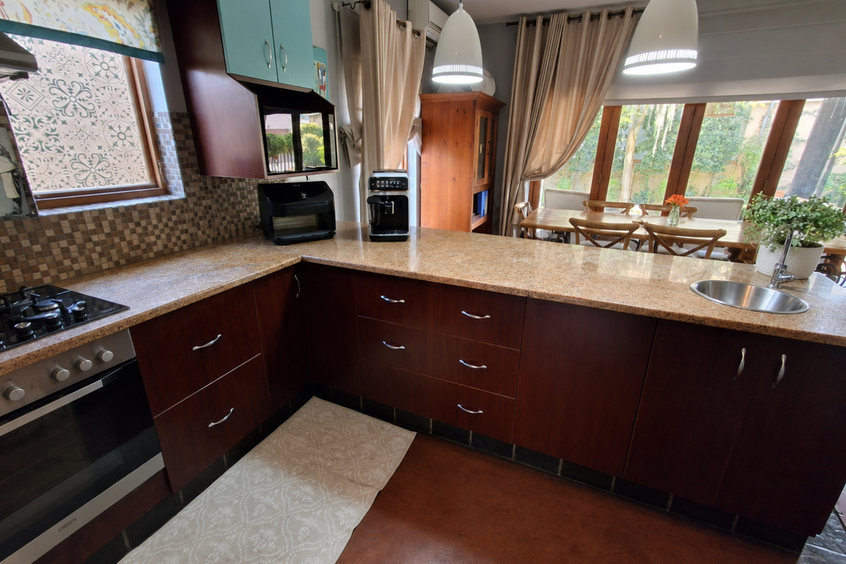 A functional kitchen featuring dark wood cabinetry, granite countertops, a built-in oven with gas hob, and a stainless steel sink overlooking the dining area.