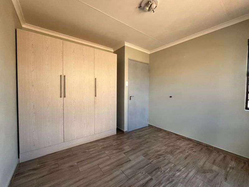 A clean, empty bedroom featuring modern wood-look tile flooring, neutral wall tones, and ample built-in cupboard storage.