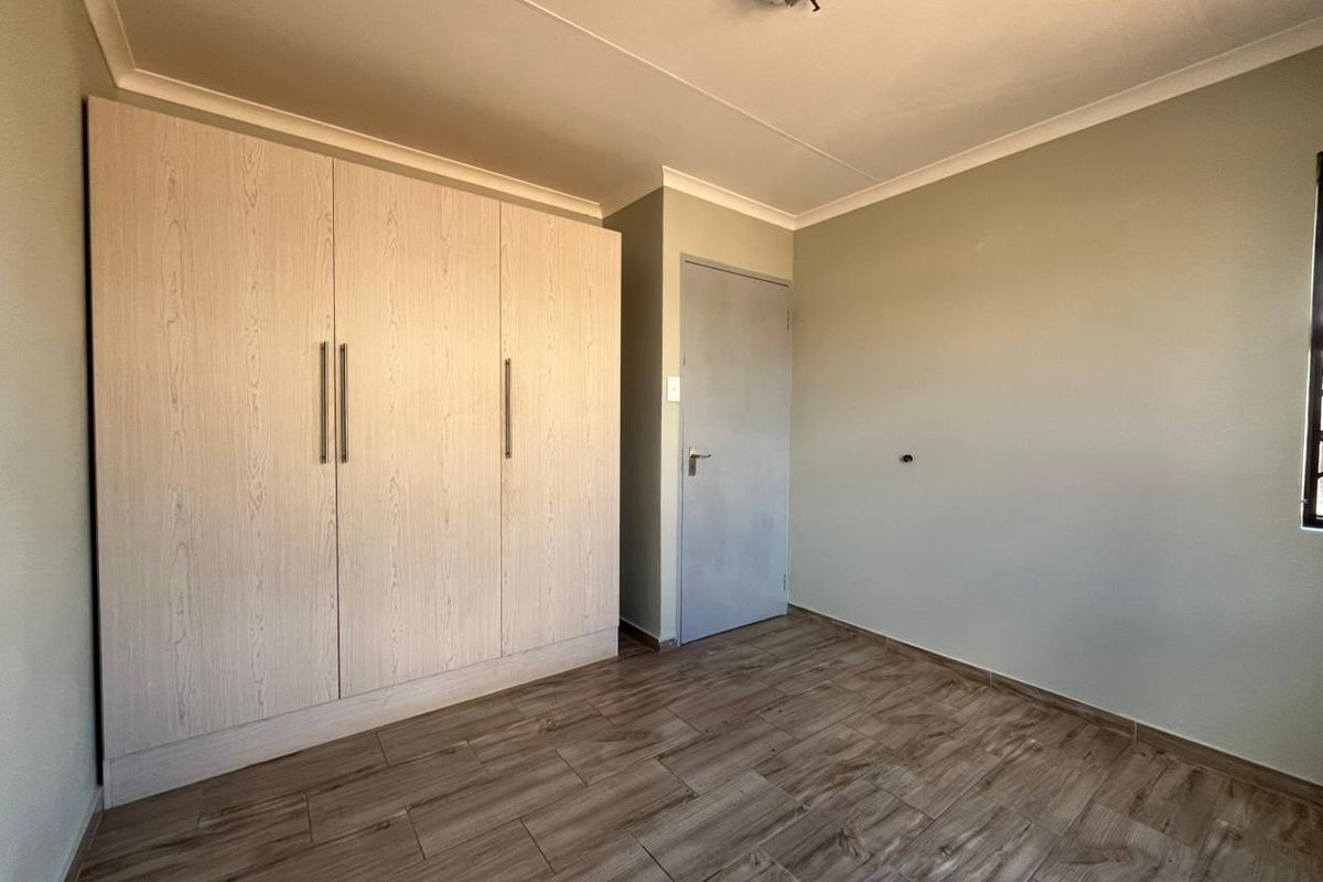 A clean, empty bedroom featuring modern wood-look tile flooring, neutral wall tones, and ample built-in cupboard storage.