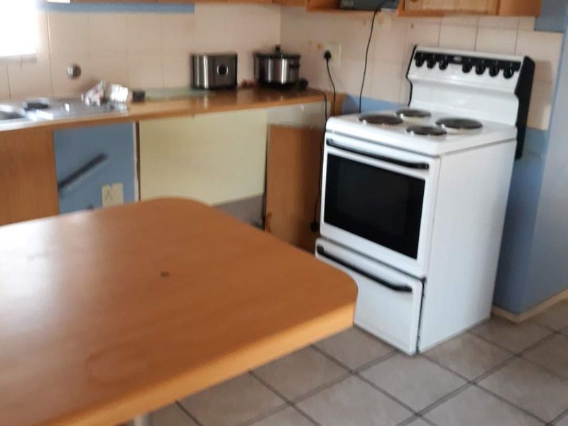 A dated kitchen featuring laminate cabinetry, tiled flooring, and a freestanding electric stove, currently requiring cosmetic updates and repairs to cabinetry.