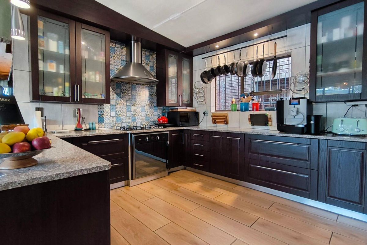 Modern kitchen featuring dark wood cabinetry, granite countertops, a gas hob with stainless steel extractor, and decorative patterned tile backsplash.