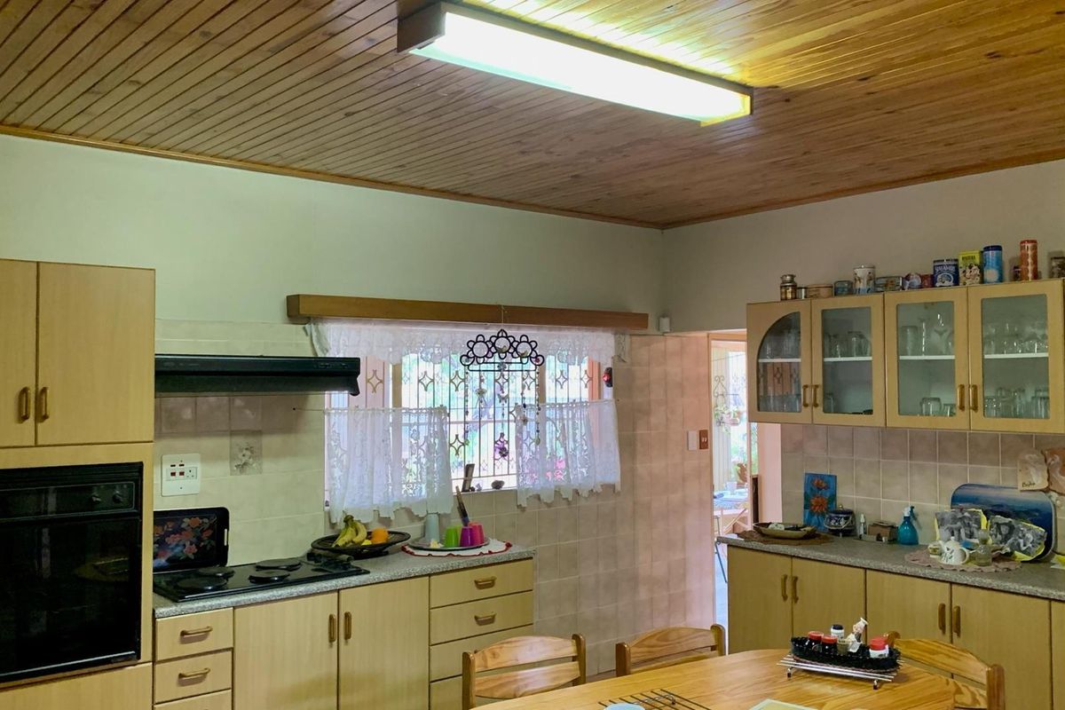 A functional kitchen featuring light wood cabinetry, built-in oven, hob, extractor fan, and a timber-clad ceiling with fluorescent lighting.