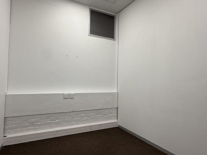 A vacant office space featuring carpeted flooring, white walls, an integrated air conditioning vent, and wall-mounted electrical outlets.