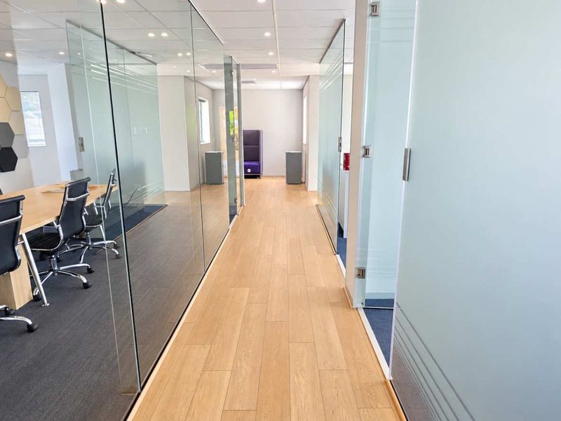 Modern office space featuring glass partition walls, acoustic wall paneling, and high-quality wood-look flooring with recessed ceiling lighting.