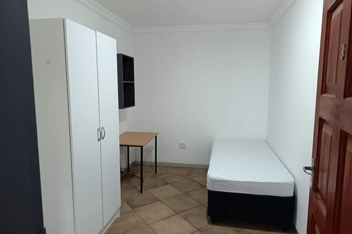 A simple bedroom featuring tiled flooring, white walls, and crown molding, providing a functional and clean living space.