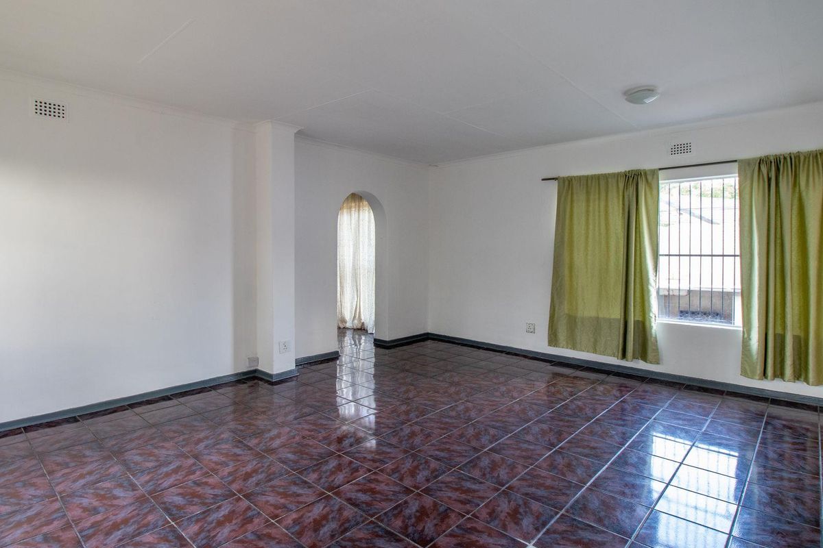 A spacious, empty living room featuring dark patterned ceramic floor tiles, white walls, and an arched doorway leading to an adjacent area.