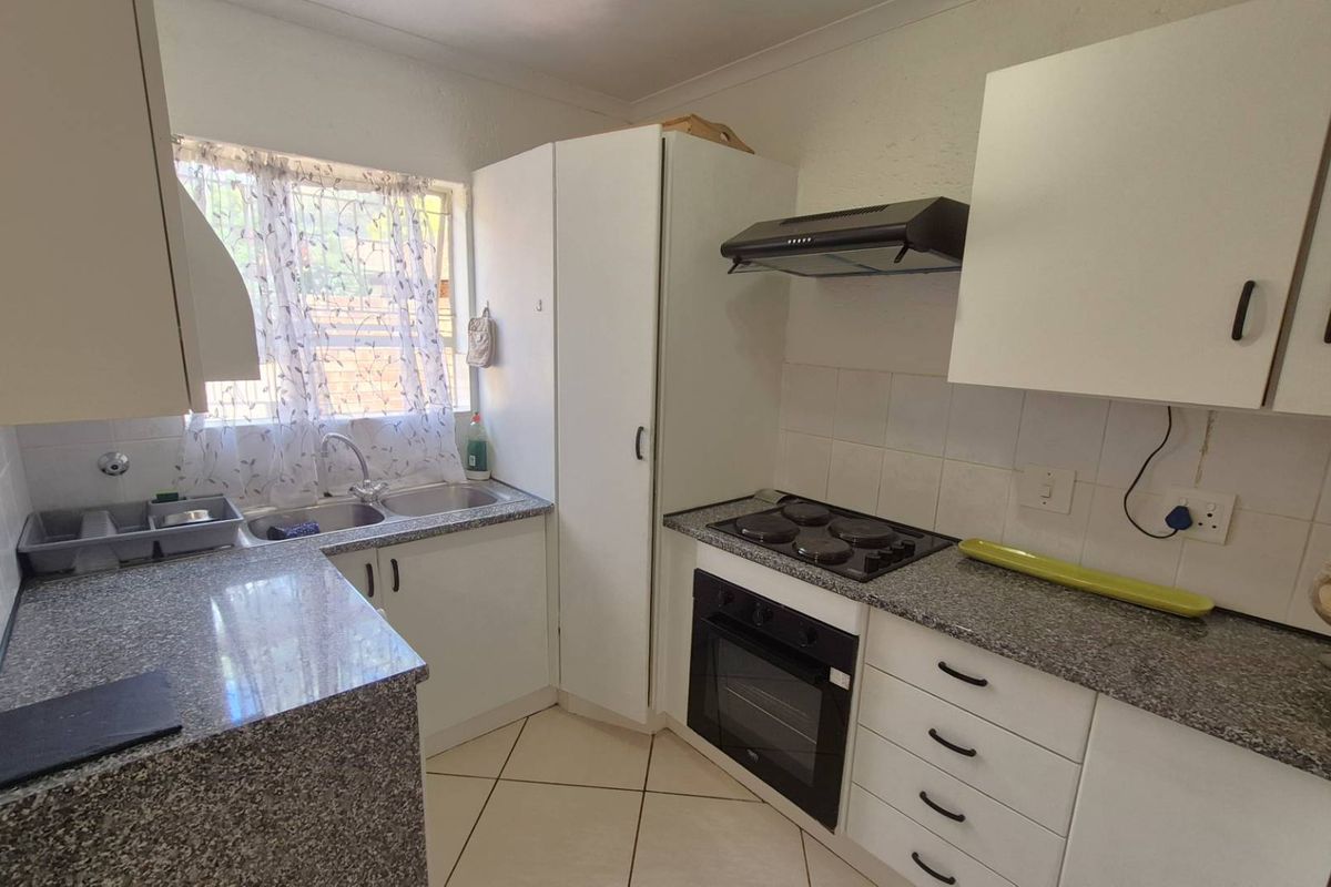 Functional kitchen featuring granite countertops, built-in oven, electric hob, extractor fan, and double basin sink with tiled flooring.