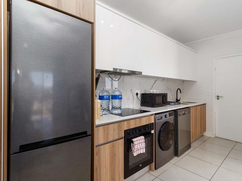Modern kitchen featuring sleek white and wood-grain cabinetry, marble-look splashback, integrated appliances, and tiled flooring.