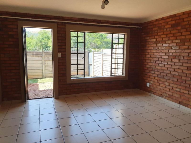 An empty living room featuring exposed brick walls, ceramic floor tiles, and direct access to the rear garden through a security-fitted door.