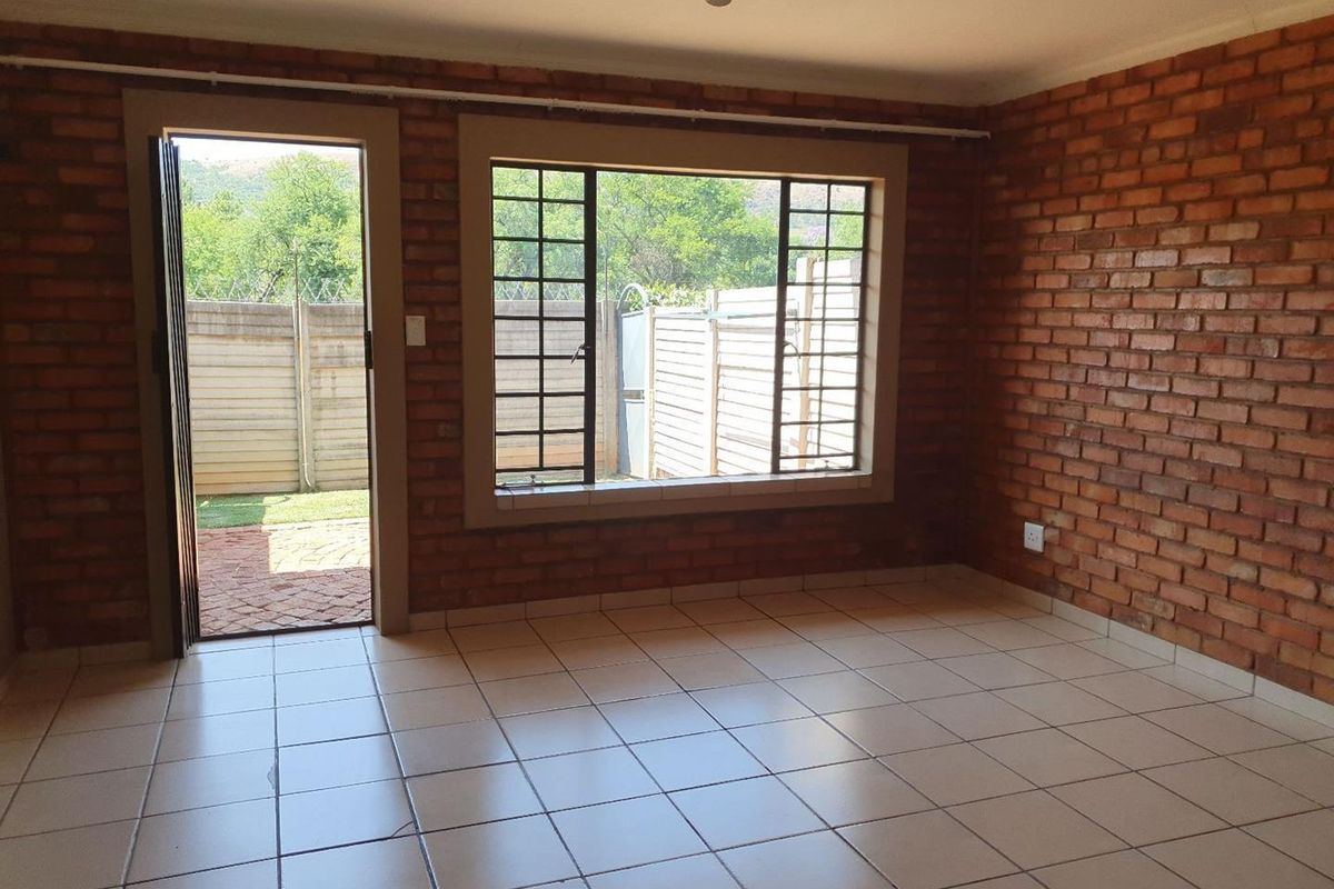 An empty living room featuring exposed brick walls, ceramic floor tiles, and direct access to the rear garden through a security-fitted door.