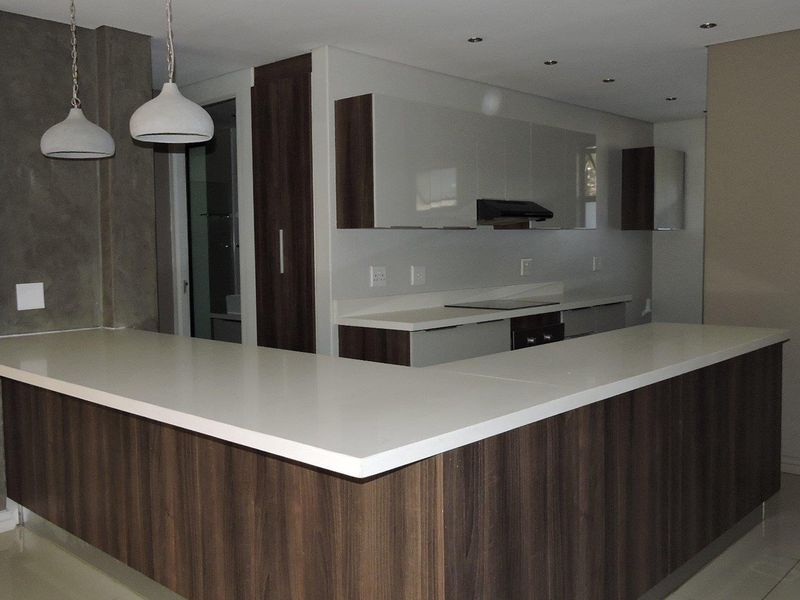 Modern kitchen featuring dark wood cabinetry, white stone countertops, a breakfast bar, and integrated appliances including a hob and extractor fan.