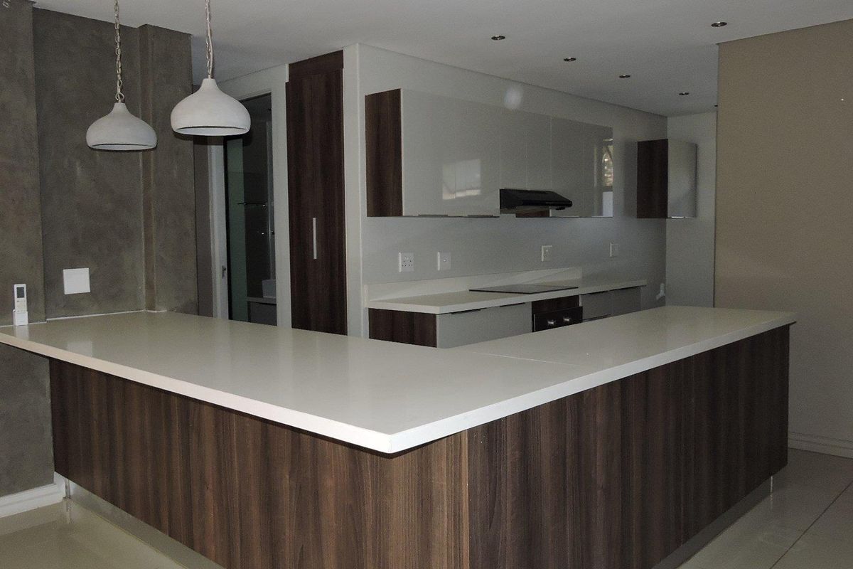 Modern kitchen featuring dark wood cabinetry, white stone countertops, a breakfast bar, and integrated appliances including a hob and extractor fan.