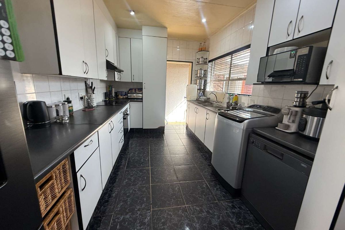 Functional galley-style kitchen featuring white cabinetry, dark countertops, tiled flooring, and integrated appliance spaces with direct access to the exterior.