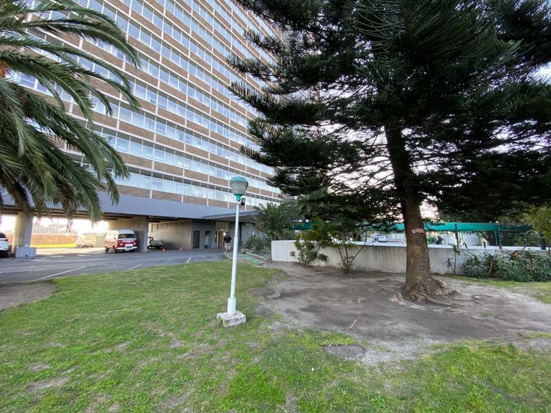 Exterior view of a multi-story apartment building featuring a paved driveway, landscaped garden area, and established trees.