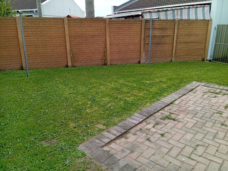 A private rear garden featuring a paved patio area, a grass lawn, and a precast concrete boundary wall.