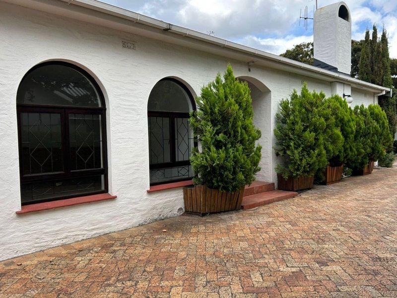 Front facade of a house featuring arched windows, a textured white masonry finish, a prominent chimney, and a brick-paved driveway.
